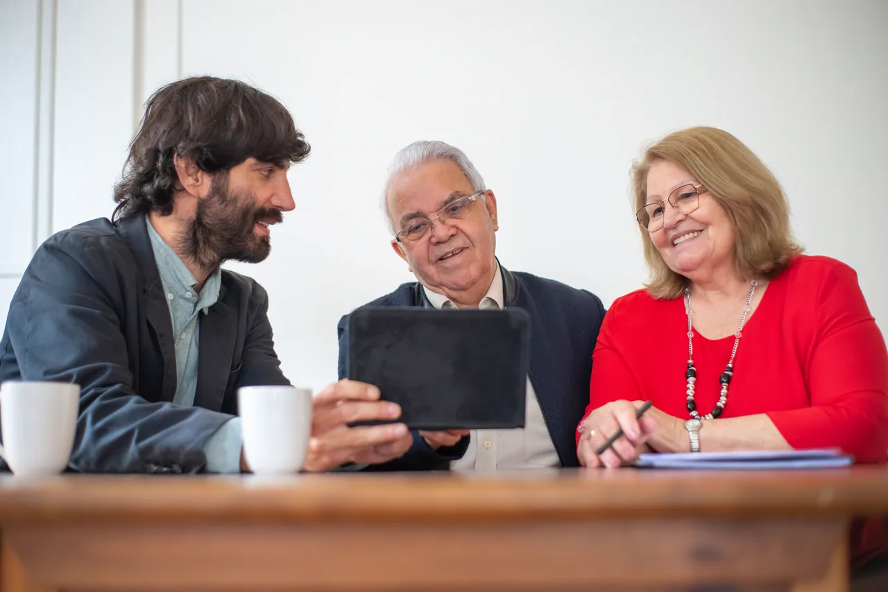 An insurance advisor shows a smiling senior couple their coverage on a tablet