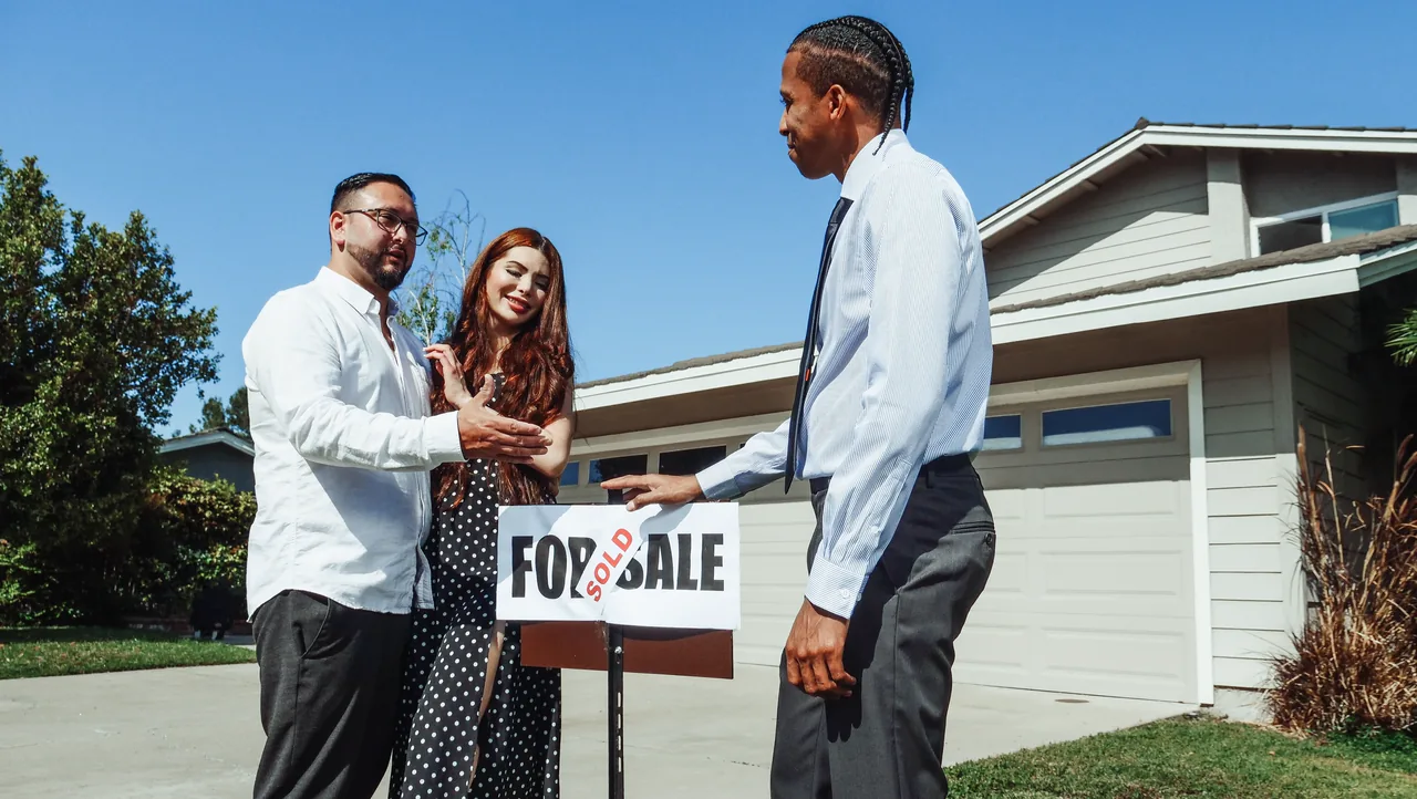 A real estate agent congratulates a couple beside a sold sign outside their new home